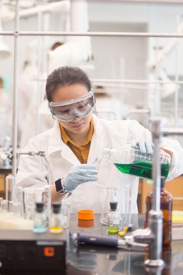 Female chemistry student pouring green liquid into small beaker